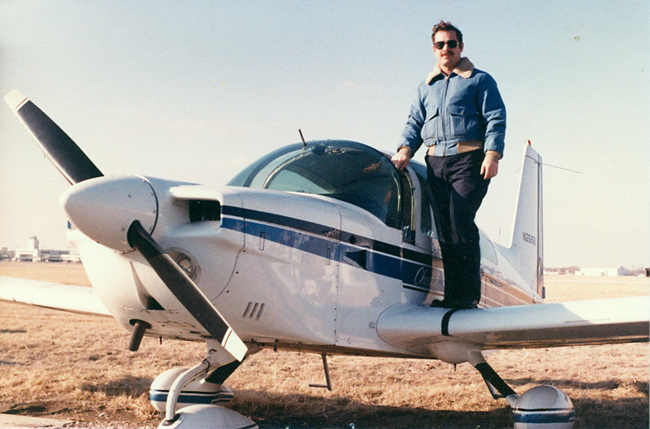Charles standing on the wing of a white with blue trim Grumman Chaeta low wing aircraft that he soloed in on February of 1981.  