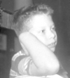 A 10 year old Charles in 1960  is seated at a metal chair and is looking back over his arm while holding his head up with his hand. He has a day dreamer look about him.